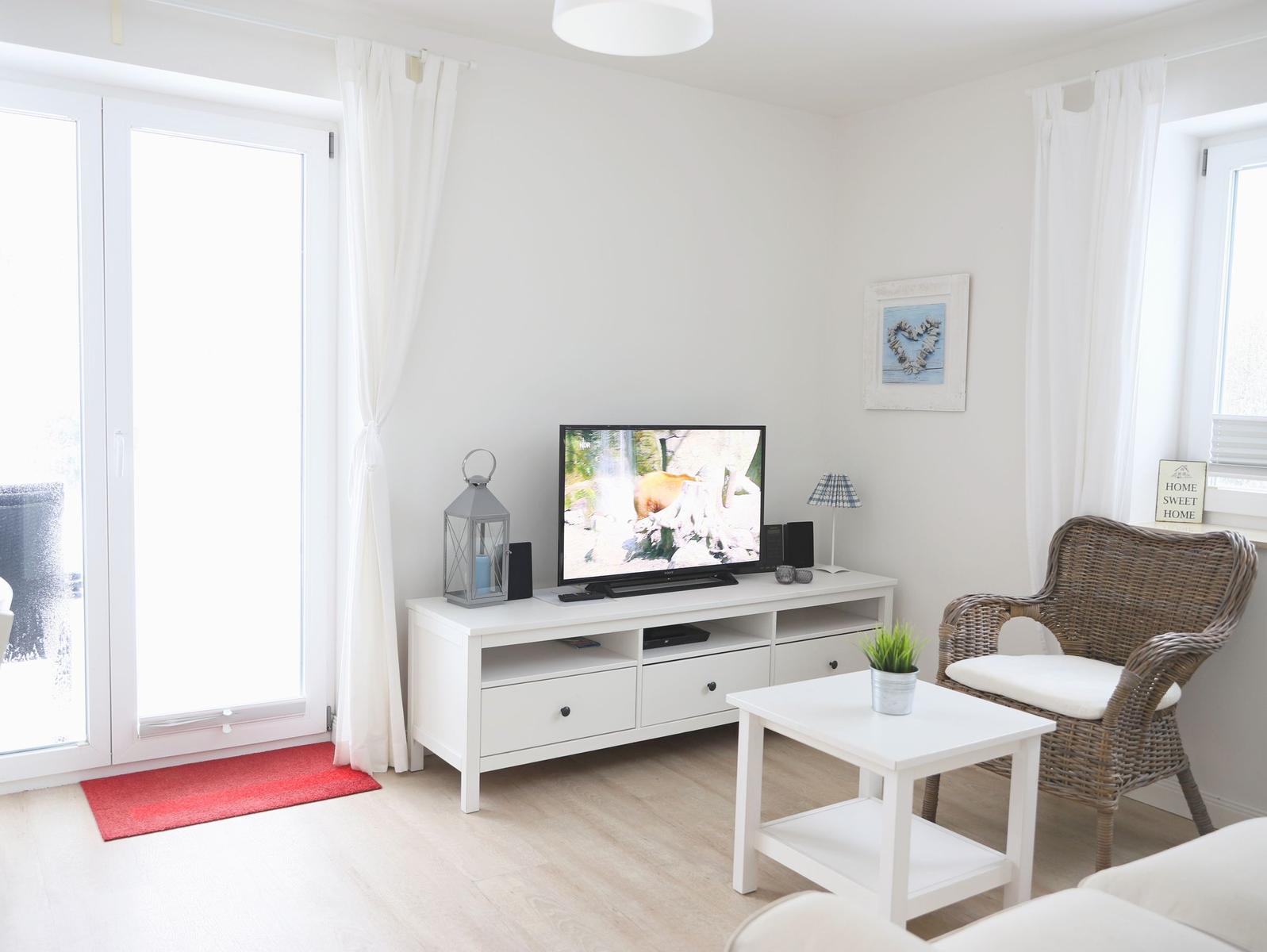 Wohnzimmer mit Fernseher, Wickerstuhl und Fenster zur Terrasse.