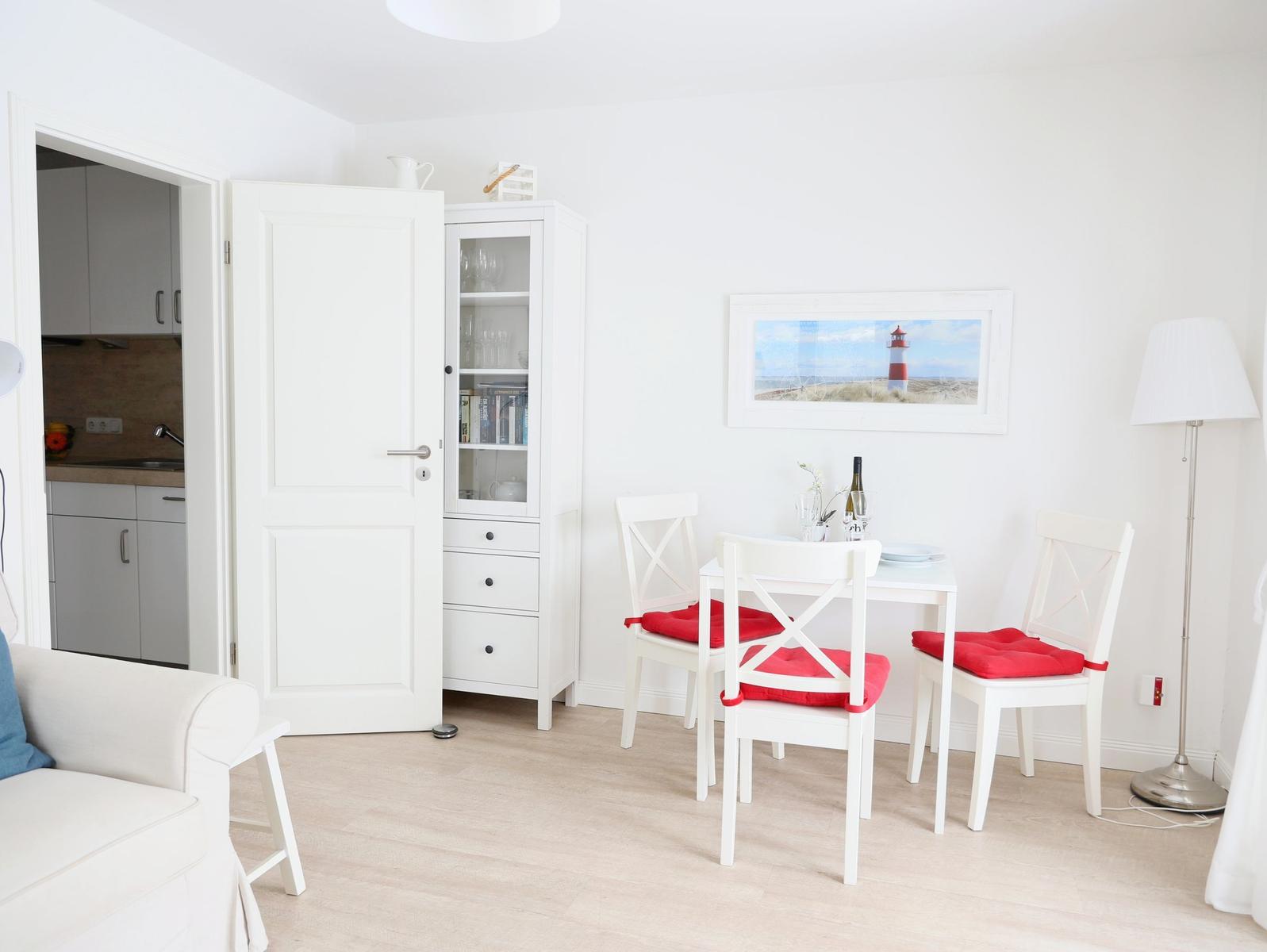 Essbereich mit weißem Tisch, drei Stühlen mit roten Sitzkissen und einer Lampe.