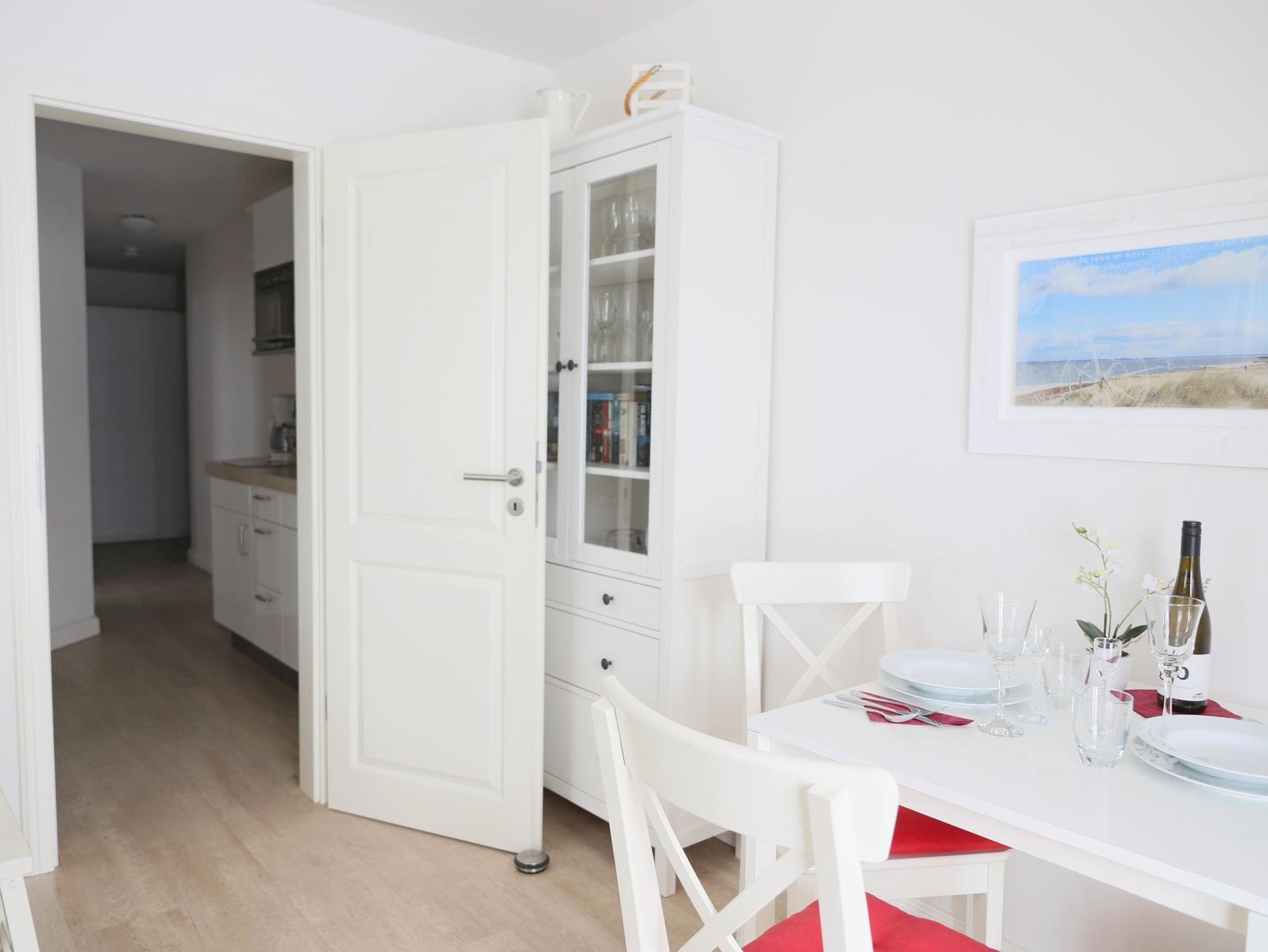 Essbereich mit weißem Tisch und Stühlen. Hintergrund zeigt Küchenbereich und Schrank.