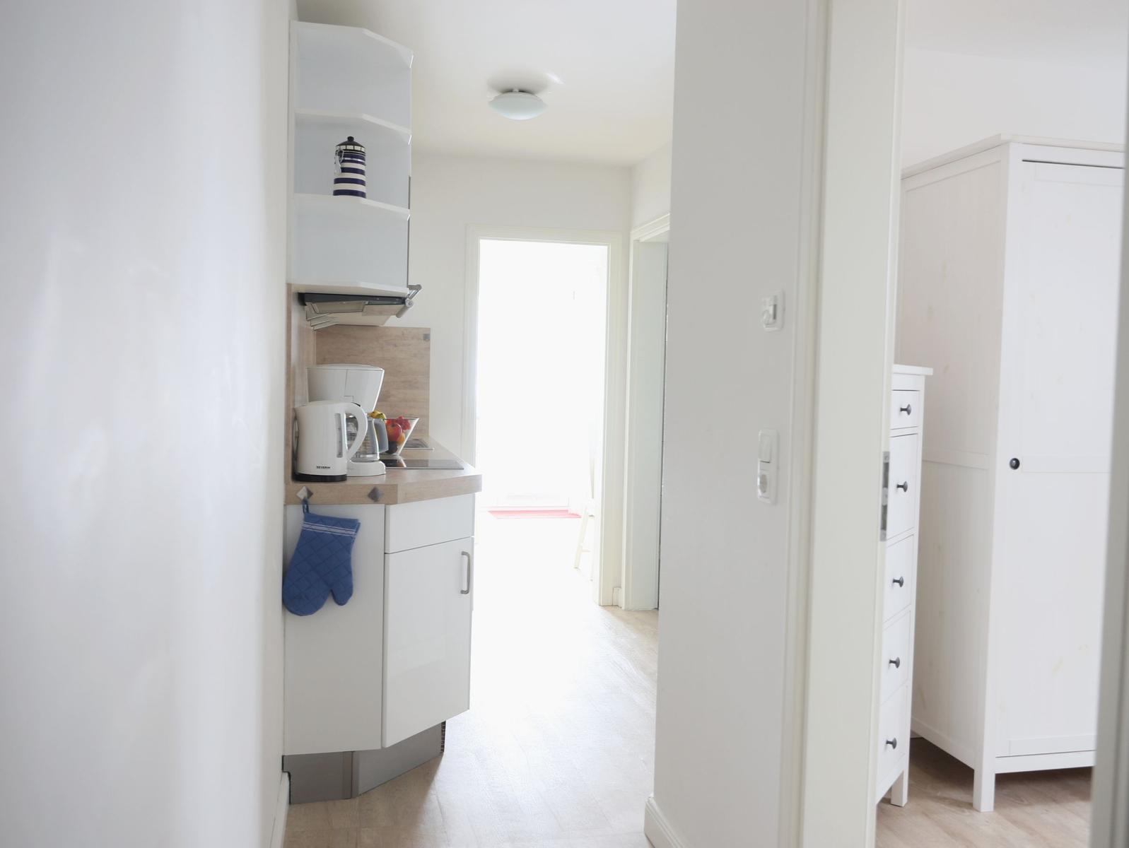 Küche mit Arbeitsfläche, Kaffeemaschine und Schrank. Blick in einen Flur mit Schrank und Tür.