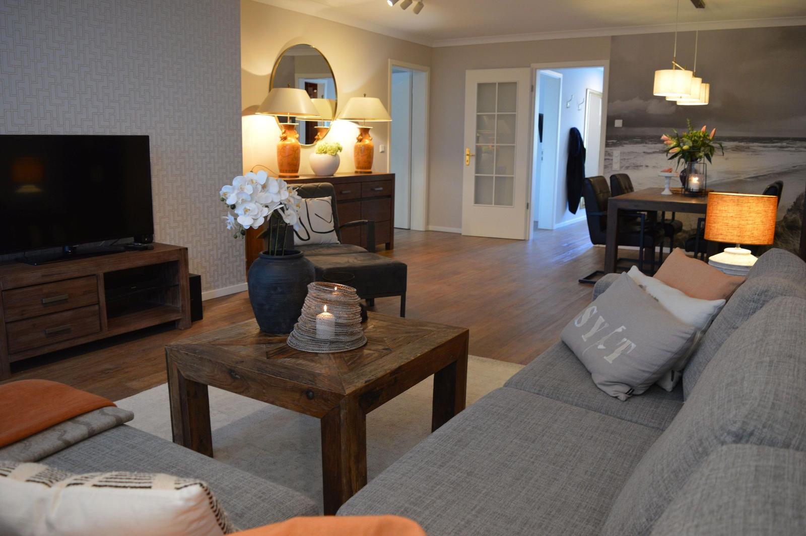 Wohnzimmer mit Sofa, Couchtisch und Fernseher. Im Hintergrund ist das Esszimmer.