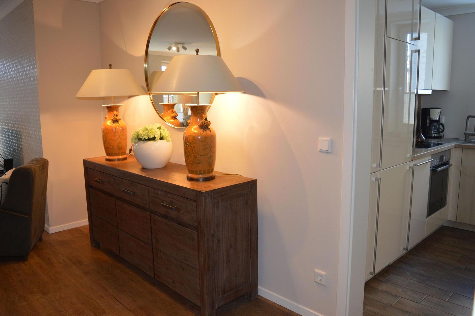 Holzschrank mit zwei Lampen und Vasen. Küche mit weißen Schränken im Hintergrund.