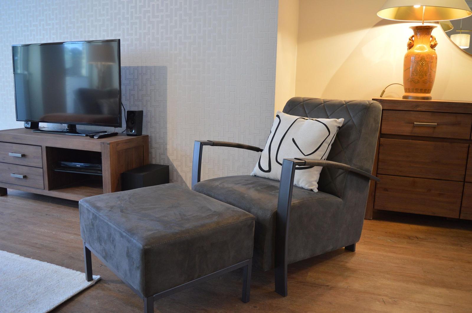 Ein grauer Sessel mit Kissen und Fußhocker vor einem Fernseher.