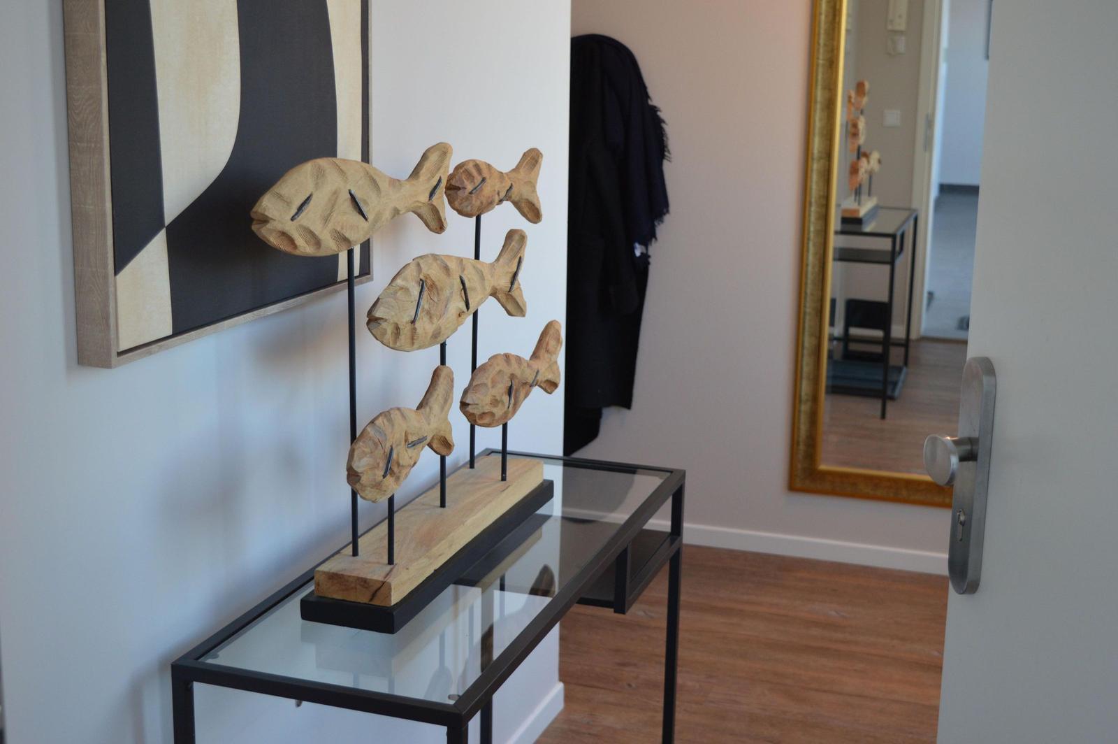 Holzfigur mit Fischen auf Glas-Tisch. Hintergrund: Wandbild und Spiegel.