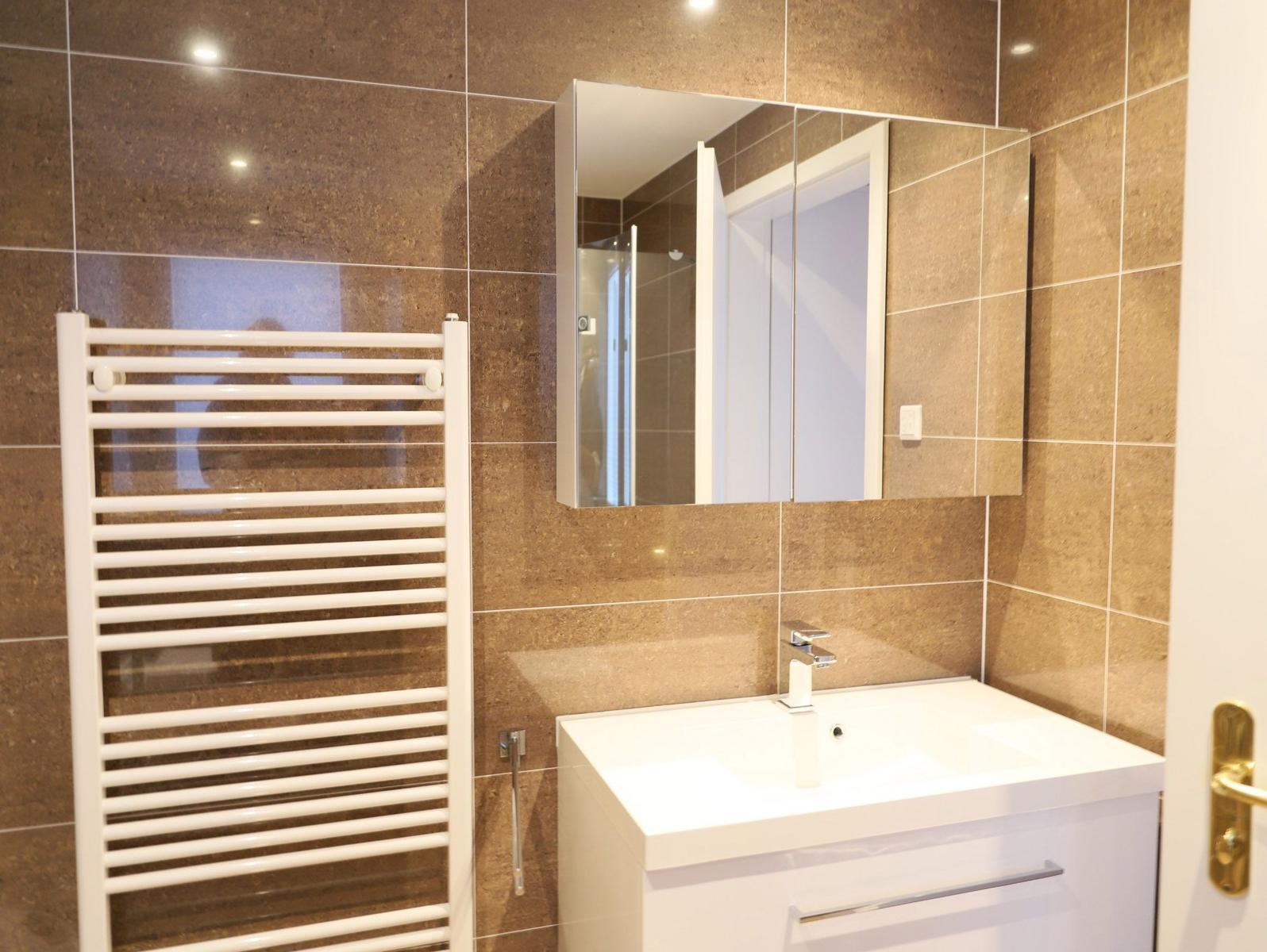 Badezimmer mit Waschbecken, Spiegelschrank und Heizkörper an braunen Fliesen.