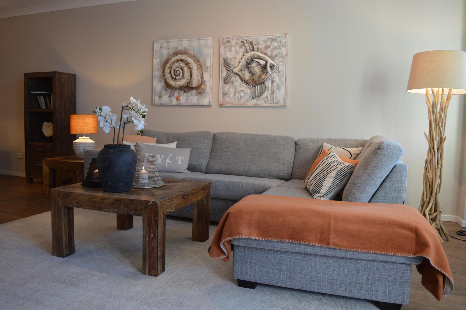Ein Wohnzimmer mit grauem Sofa, rustikalem Tisch und Wandbildern.