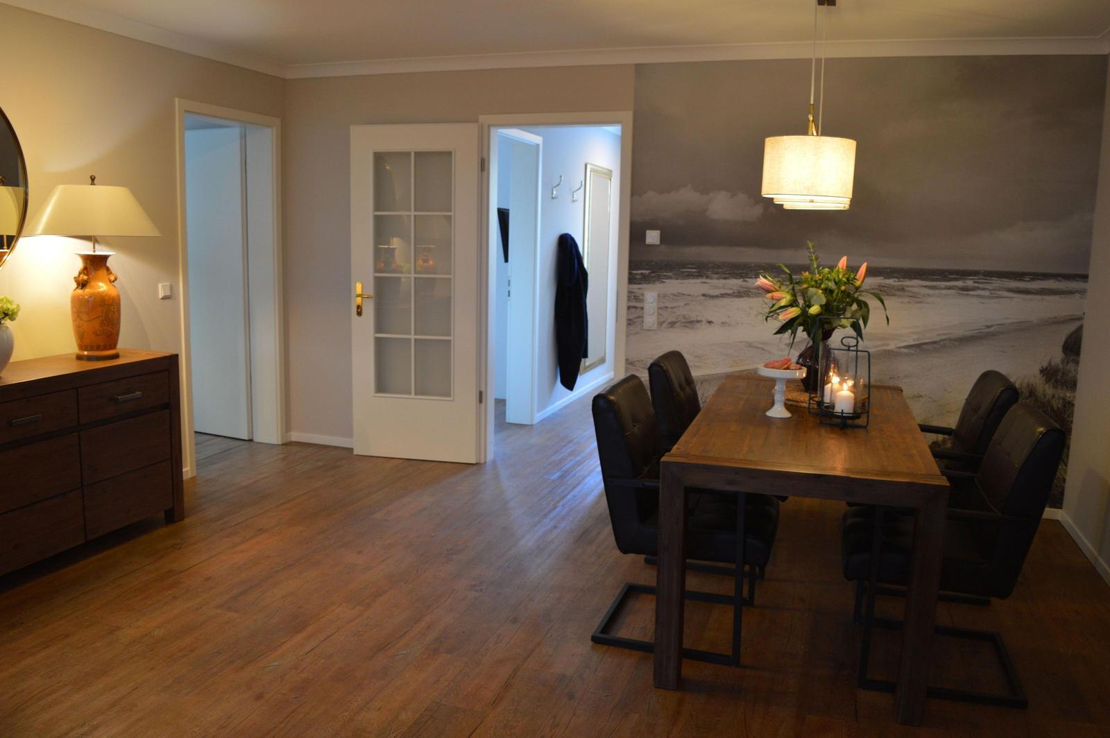 Essbereich mit Holztisch, schwarzen Stühlen und Wandbild. Holzfußboden und Türen sind sichtbar.