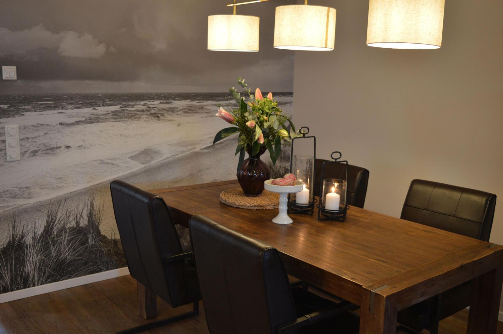 Esszimmer mit Holztisch, schwarzen Stühlen und Wandbild von Strand.