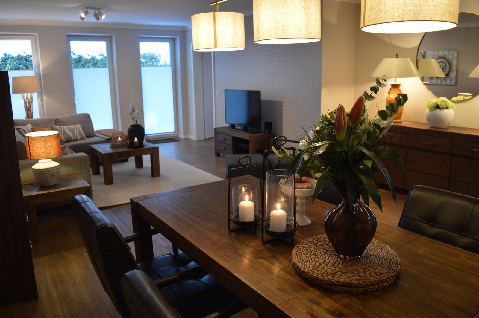 Esszimmer mit Holztisch und Stühlen, Wohnzimmer mit Sofa und Fernseher im Hintergrund.