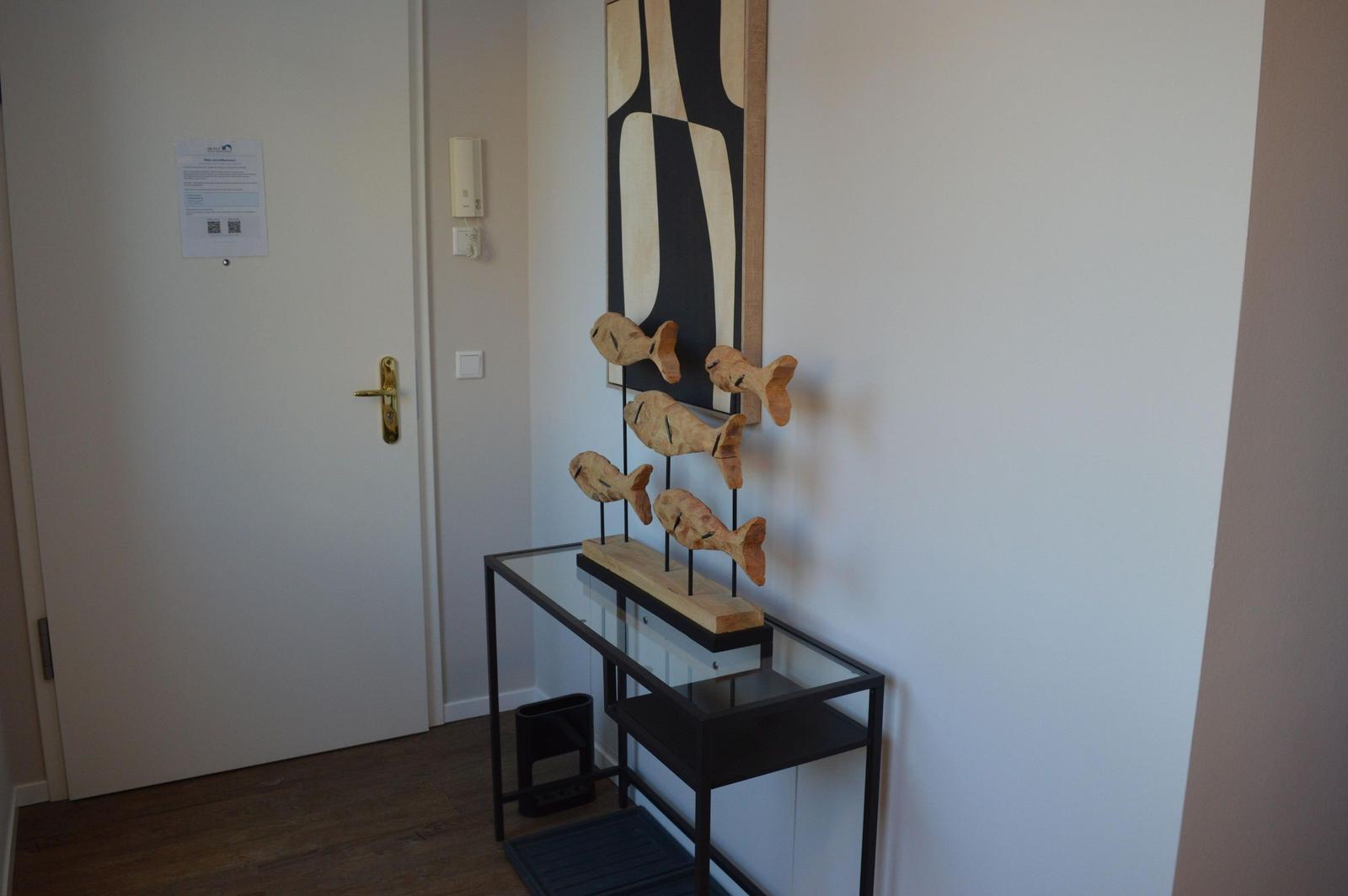 Eingangsbereich mit Holztisch, dekorativen Fischfiguren und Wandbild.