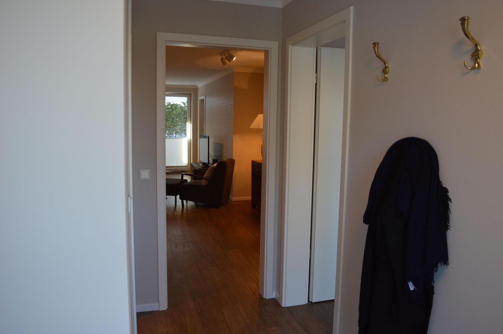 Hausgang mit Kleiderhaken und Blick in Wohnzimmer mit Sessel und Fenster.