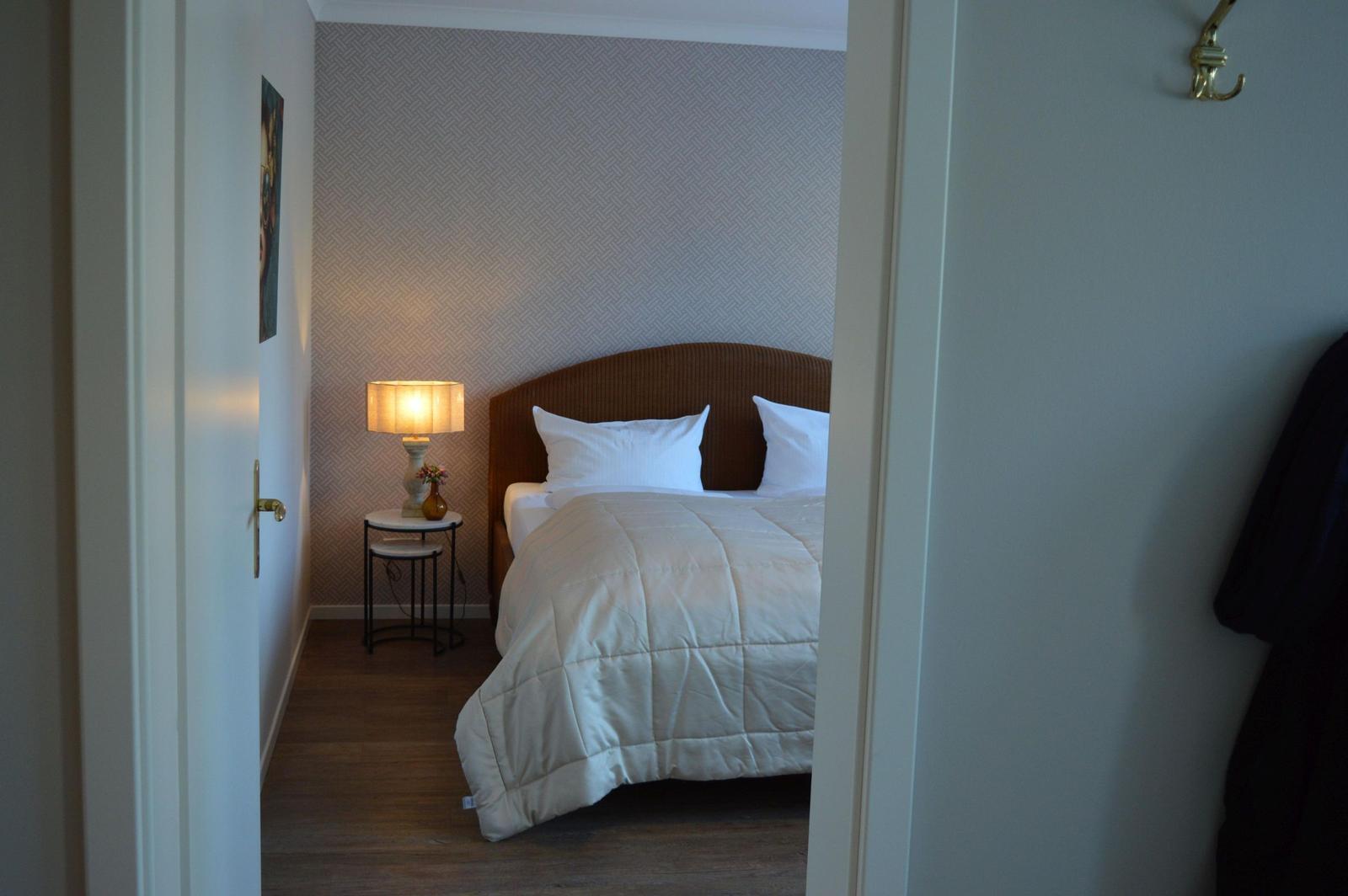 Schlafzimmer mit Bett, Nachttisch und Lampe. Wand mit Muster. Holzfußboden.