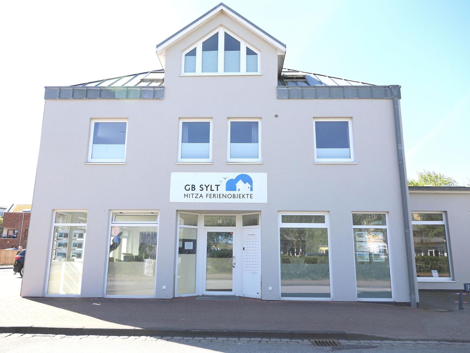 Ferienhausagentur mit Glasfassade und Schild GB Sylt. Eingang mit Tür und Fenstern.