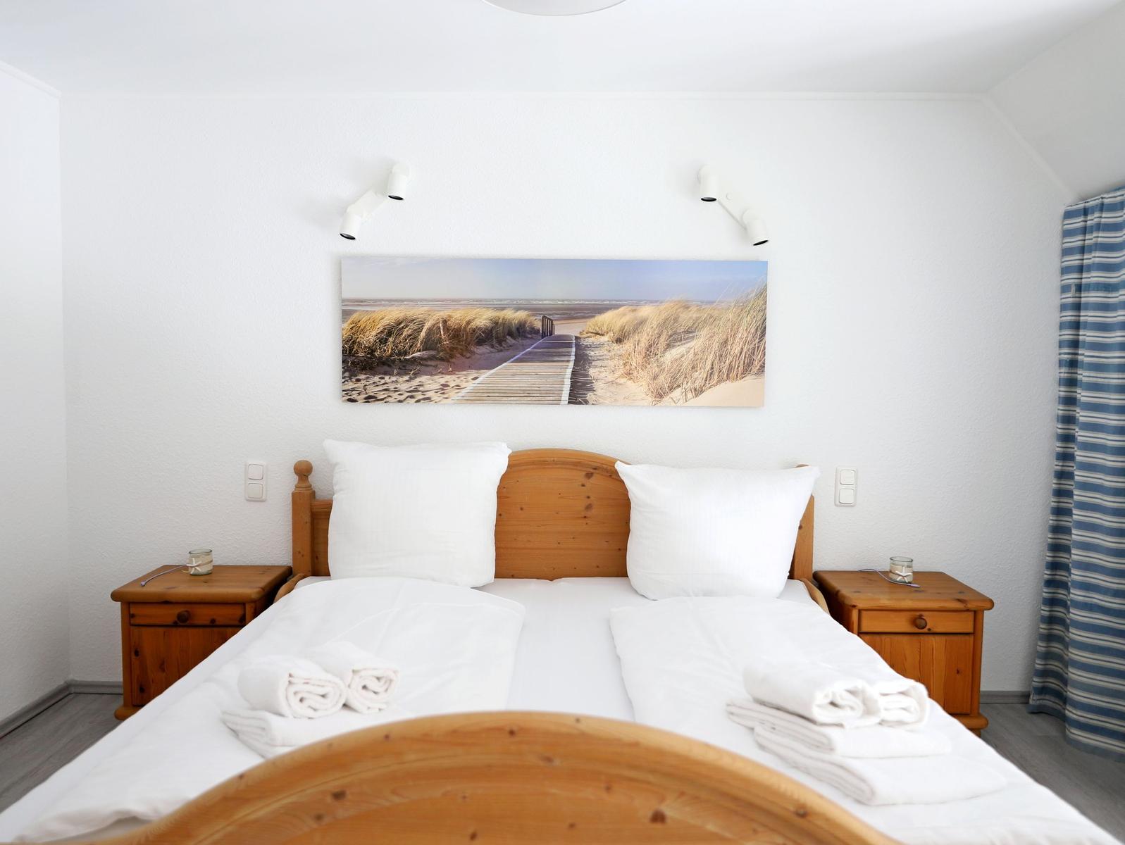 Schlafzimmer mit Holzbett, Nachttischen und Strandbild an der Wand.