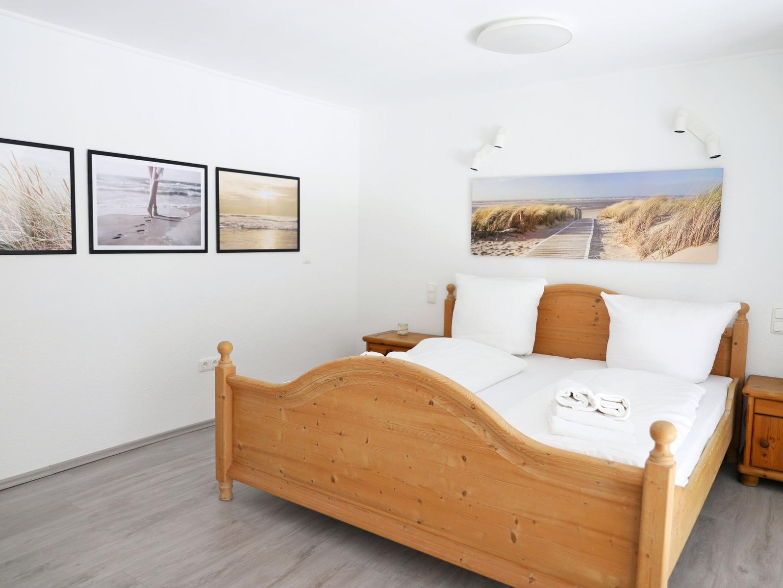 Ein Schlafzimmer mit Holzbett, weißen Kissen und Strandbildern an den Wänden.