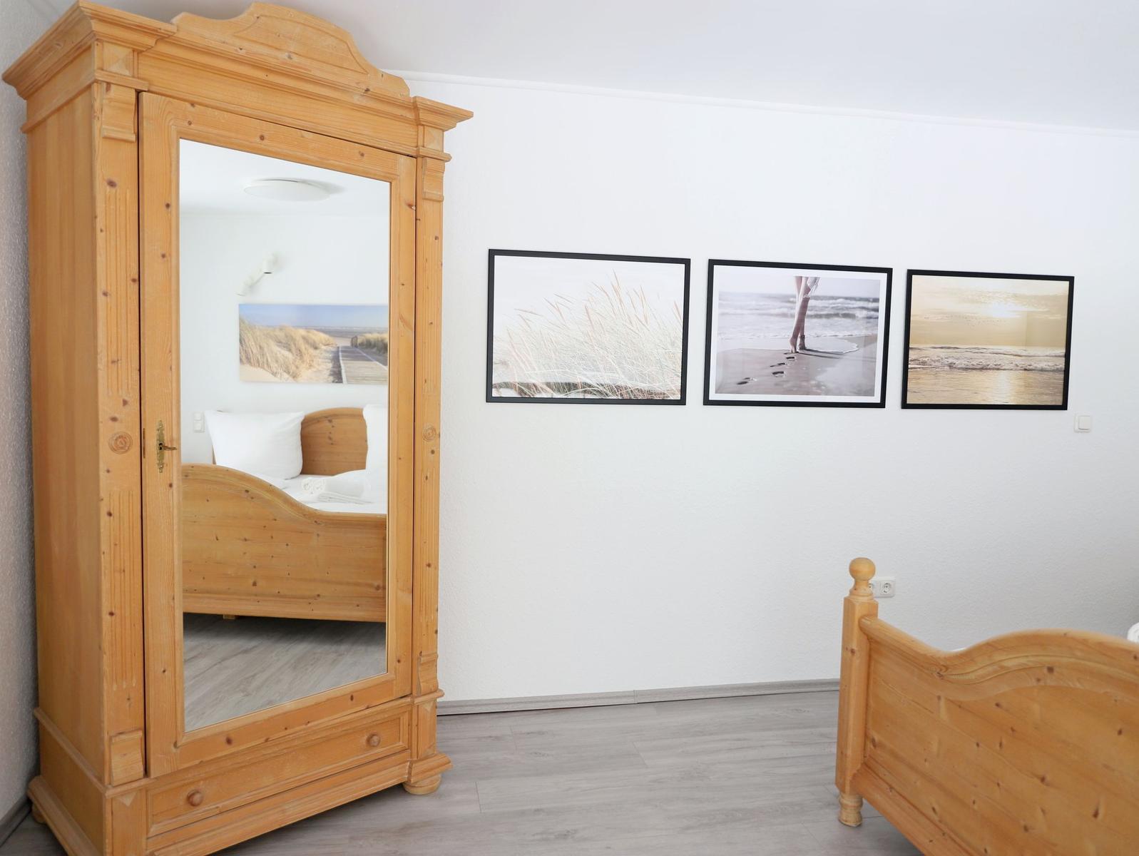 Schlafzimmer mit Holzbett, Spiegelschrank und drei Strandbildern an der Wand.