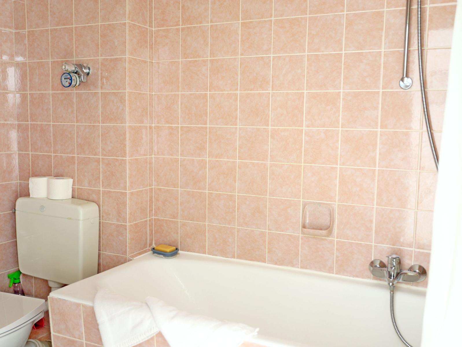 Bad mit Badewanne, Toilette und Dusche. Wände sind mit rosa Fliesen verkleidet.