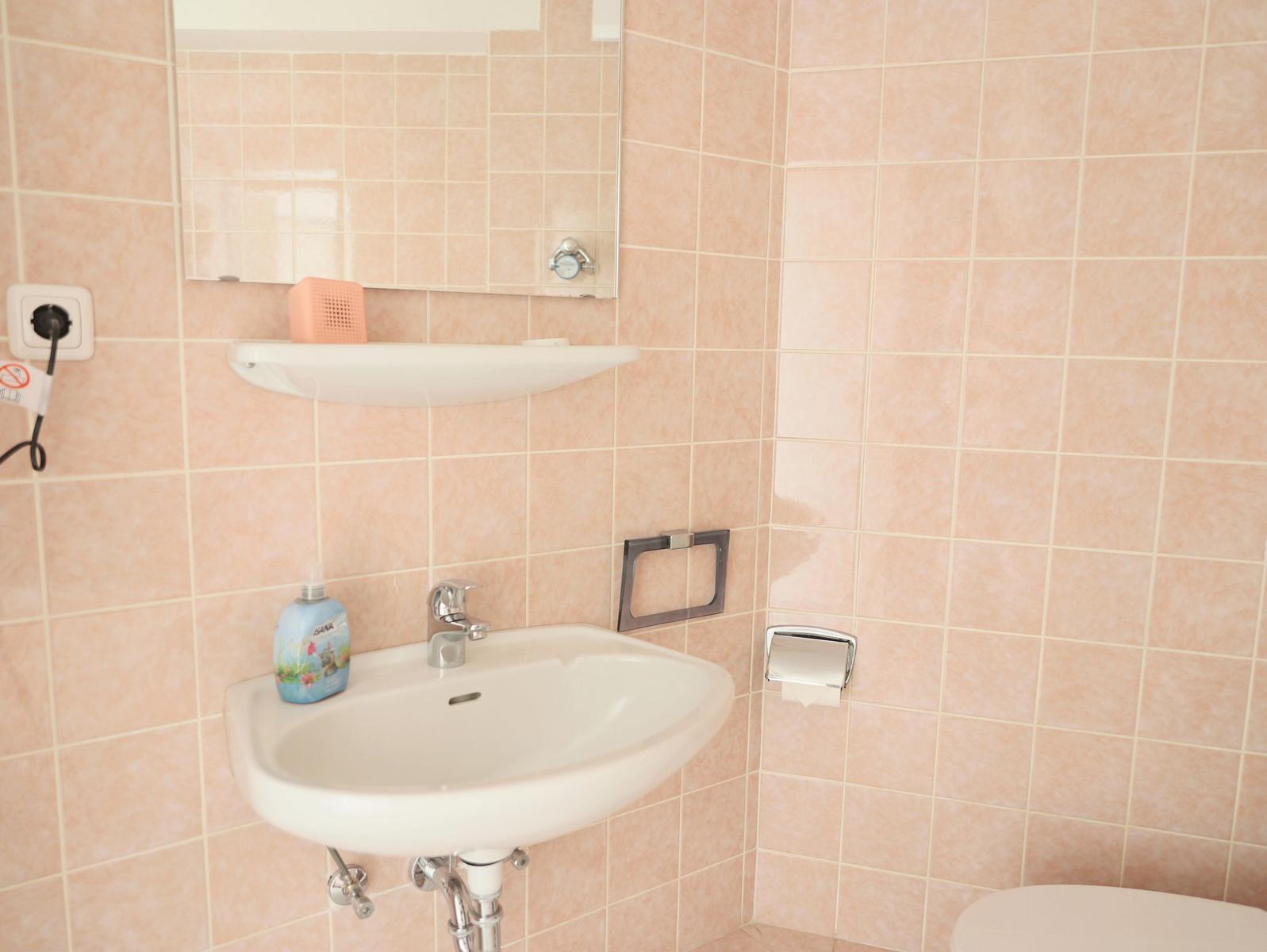 Badezimmer mit Waschbecken, Spiegel und Toilette an rosa Fliesenwand