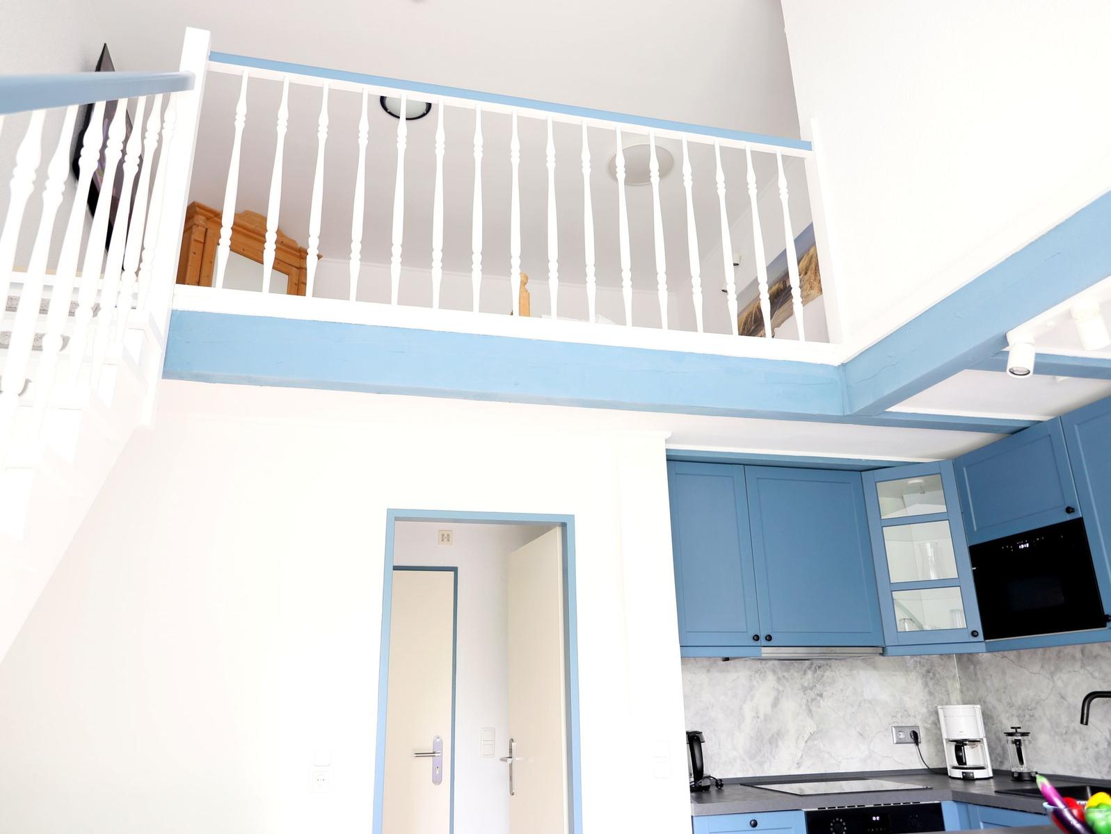 Küche mit blauen Schränken und obere Etage mit weißem Geländer.