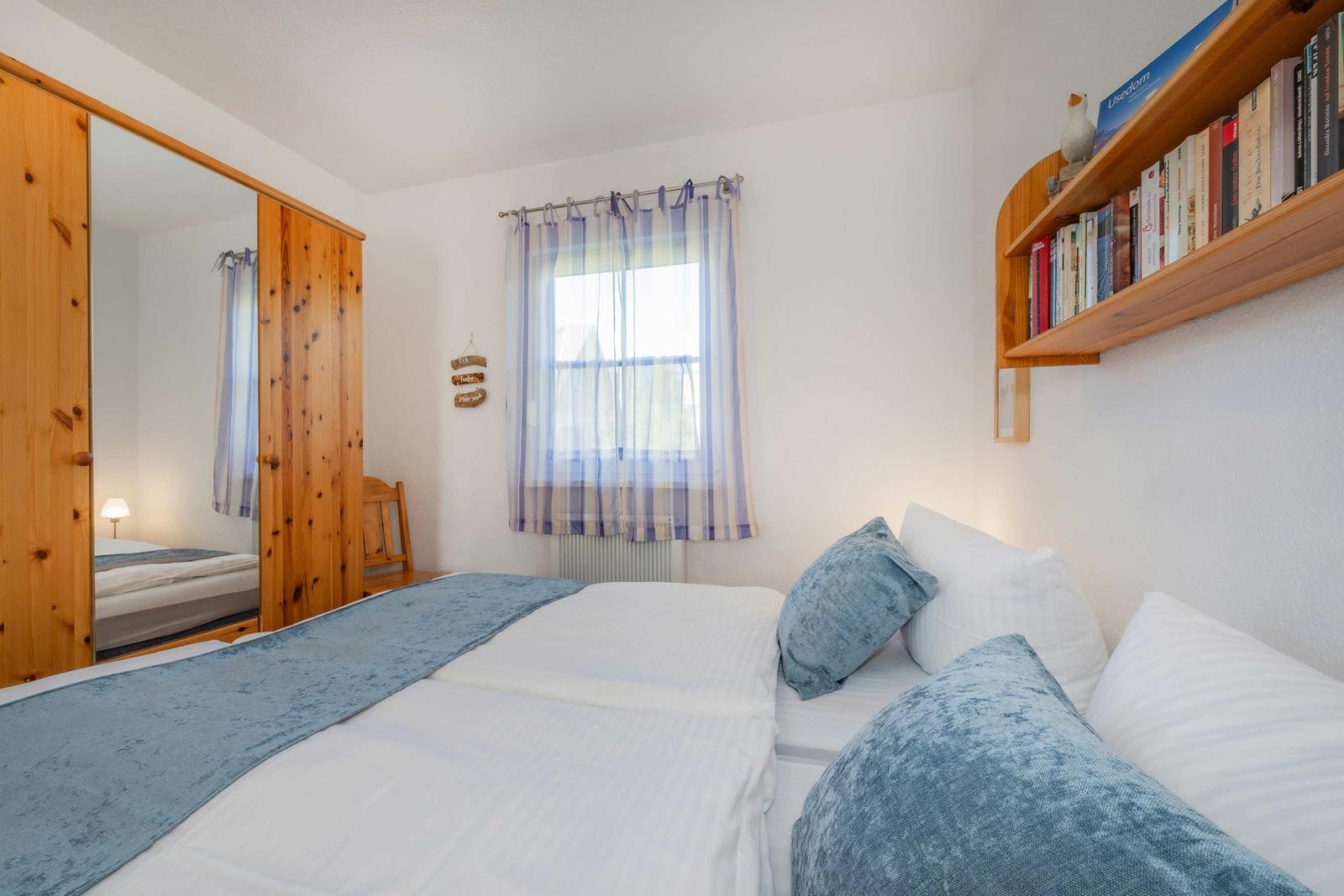 Schlafzimmer mit Bett, Kleiderschrank und Fenster mit Vorhängen.