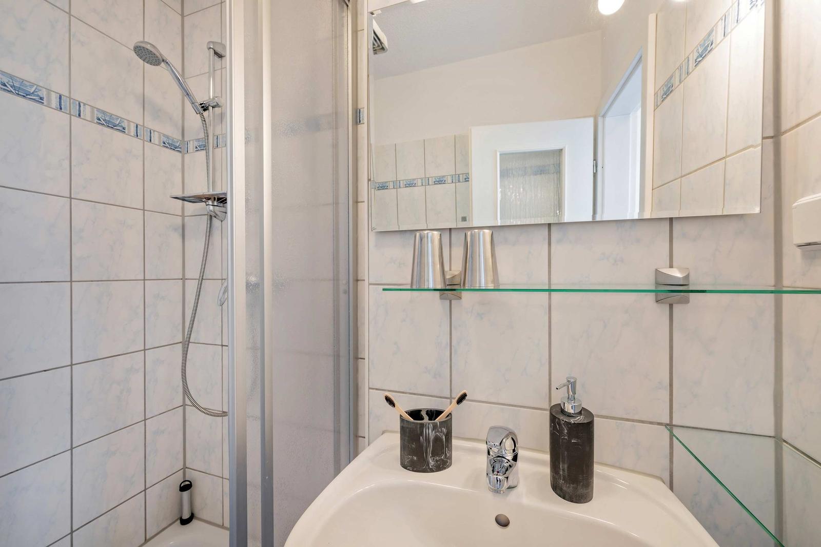 Badezimmer mit Dusche, Waschbecken und Spiegel.