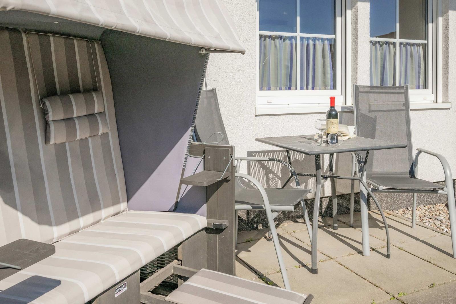 Terrasse mit Liegestuhl, Tisch und Stühlen. Flasche Wein und Gläser stehen bereit.