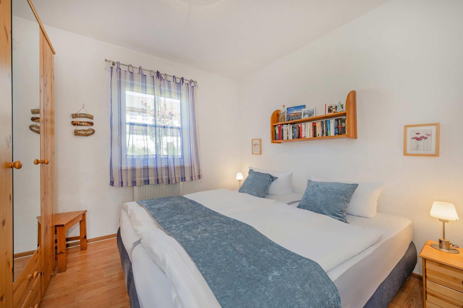 Schlafzimmer mit Bett, Kleiderschrank und Fenster mit Vorhängen.