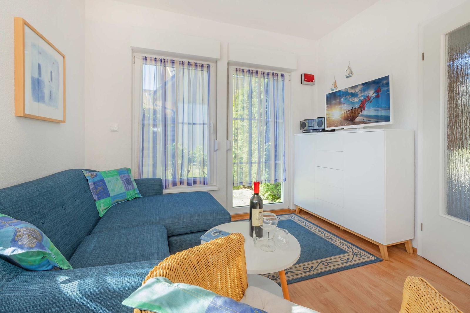 Ein Wohnzimmer mit blauem Sofa, TV und Fenstern mit Vorhängen.