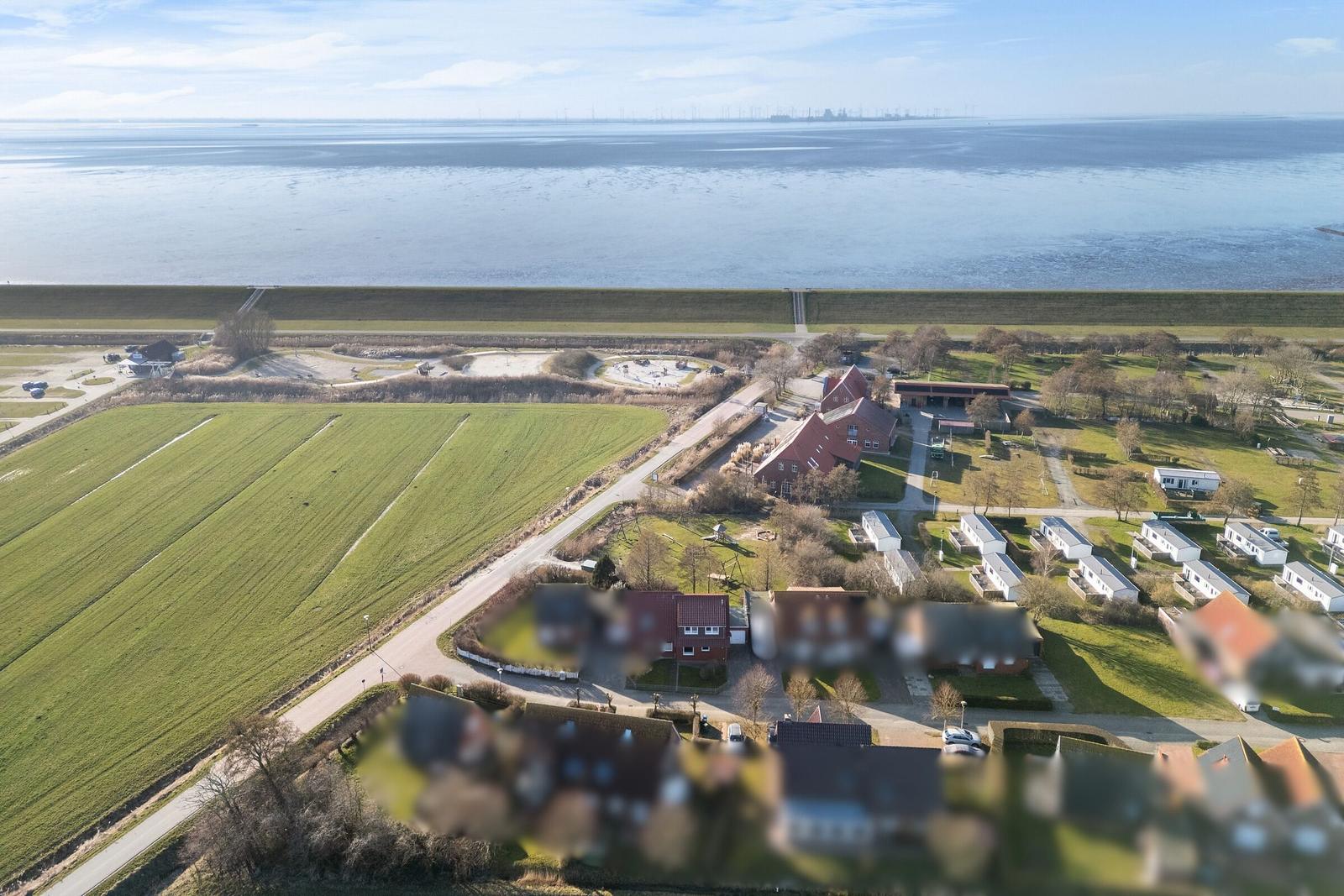 Luftbild einer Küstenlandschaft mit Feldern, Häusern und einem Deich am Wasser.
