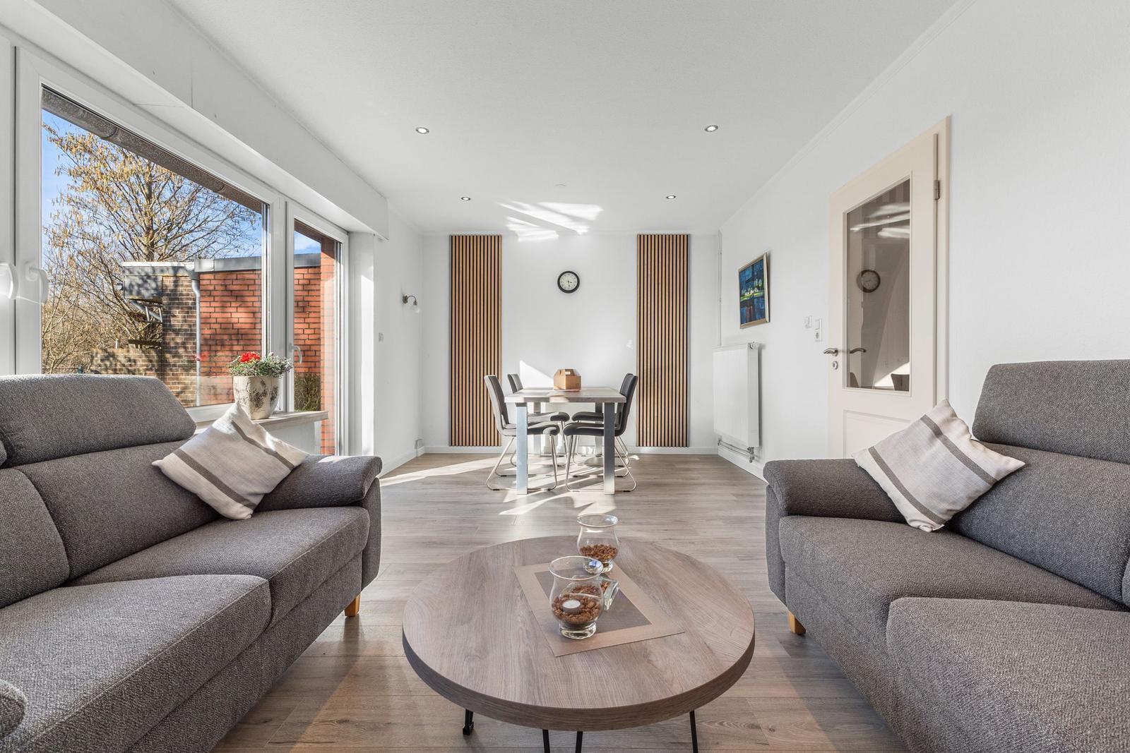 Wohn- und Essbereich mit zwei Sofas, runden Tisch und großem Fenster.