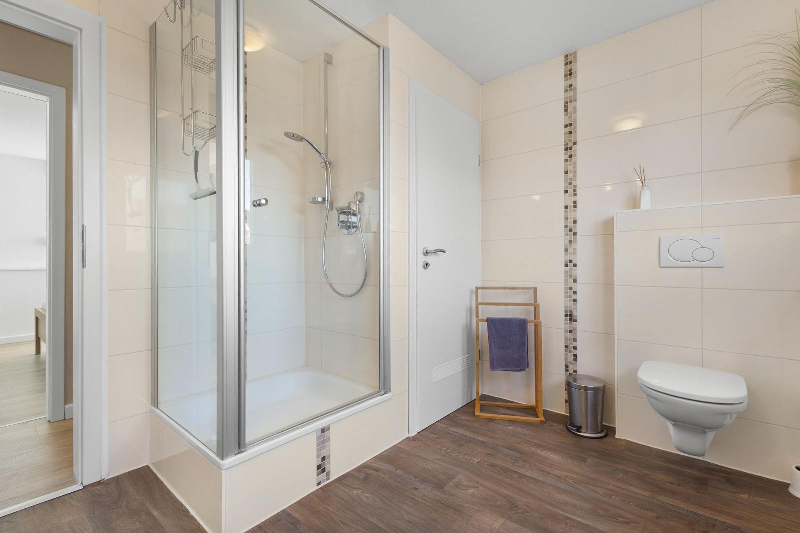 Badezimmer mit Dusche, Toilette und Holzboden.