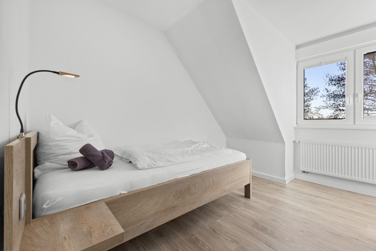 Schlafzimmer mit Dachschrägen, Holzbett, Fenster und Heizkörper.