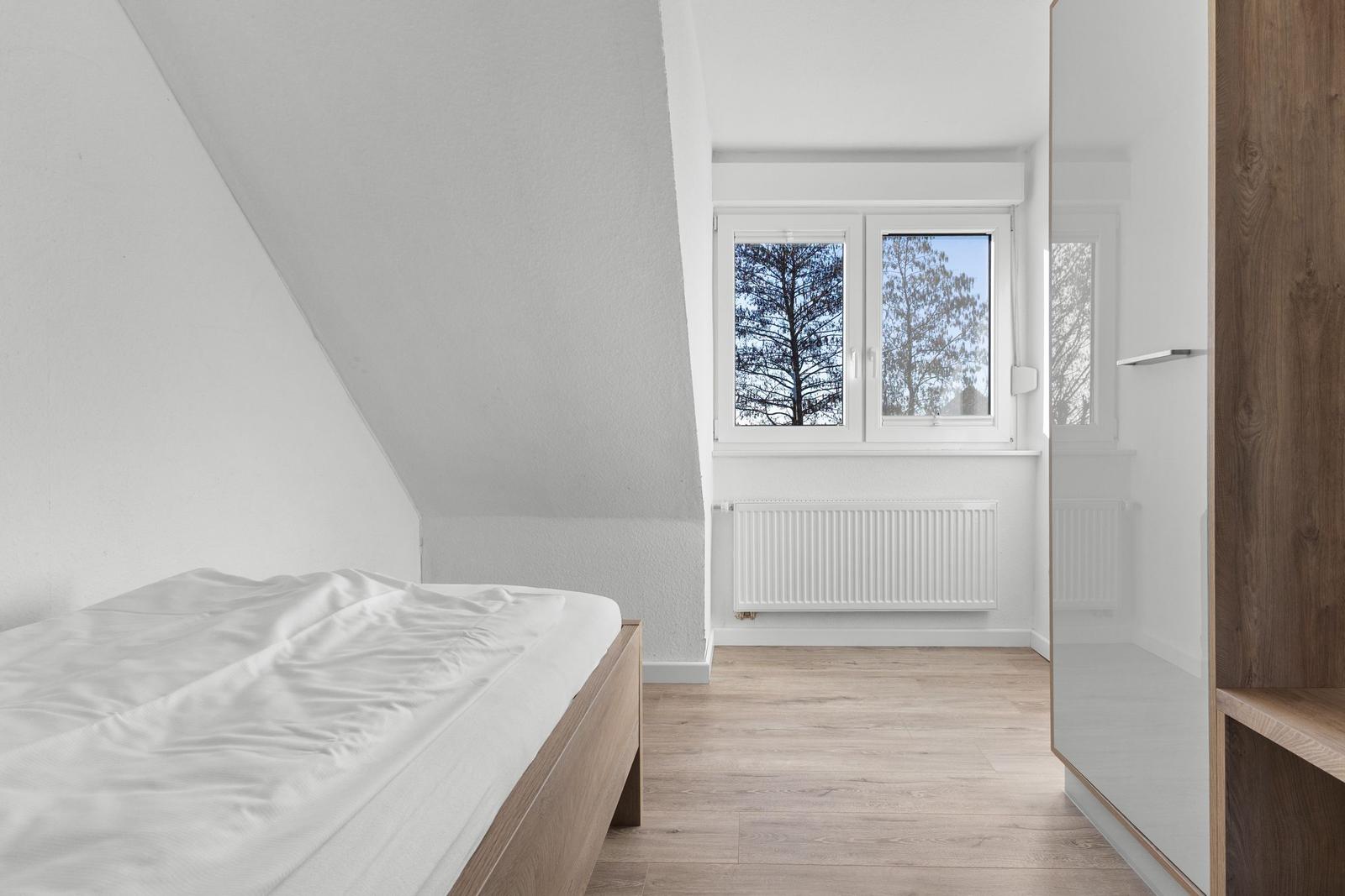 Schlafzimmer mit Dachschrägen, Bett, Fenster und Holzboden.