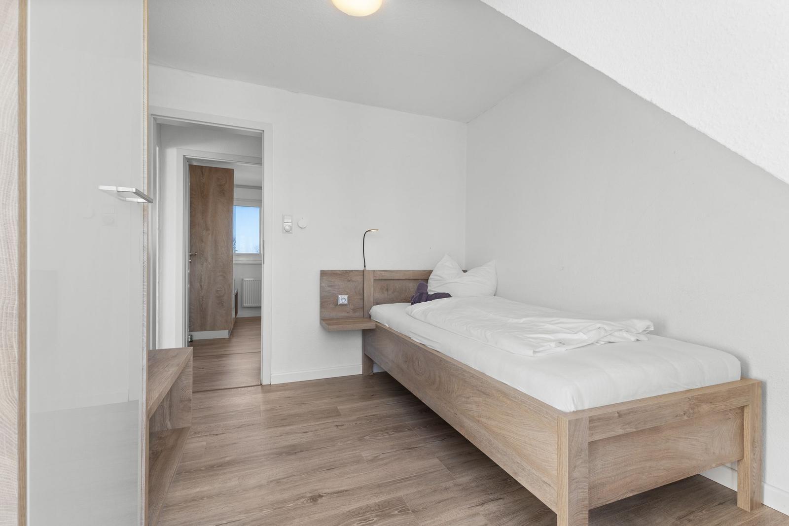 Ein Schlafzimmer mit einem Bett, Holzboden und einer Tür zum Flur.