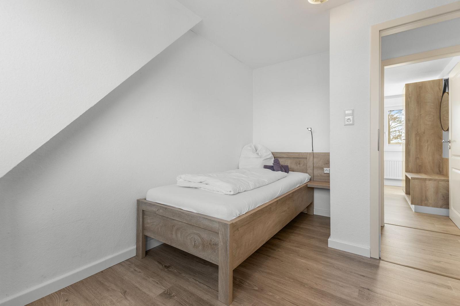 Ein Schlafzimmer mit einem Bett und einem Holzboden. Durchgang zur Badezimmer.