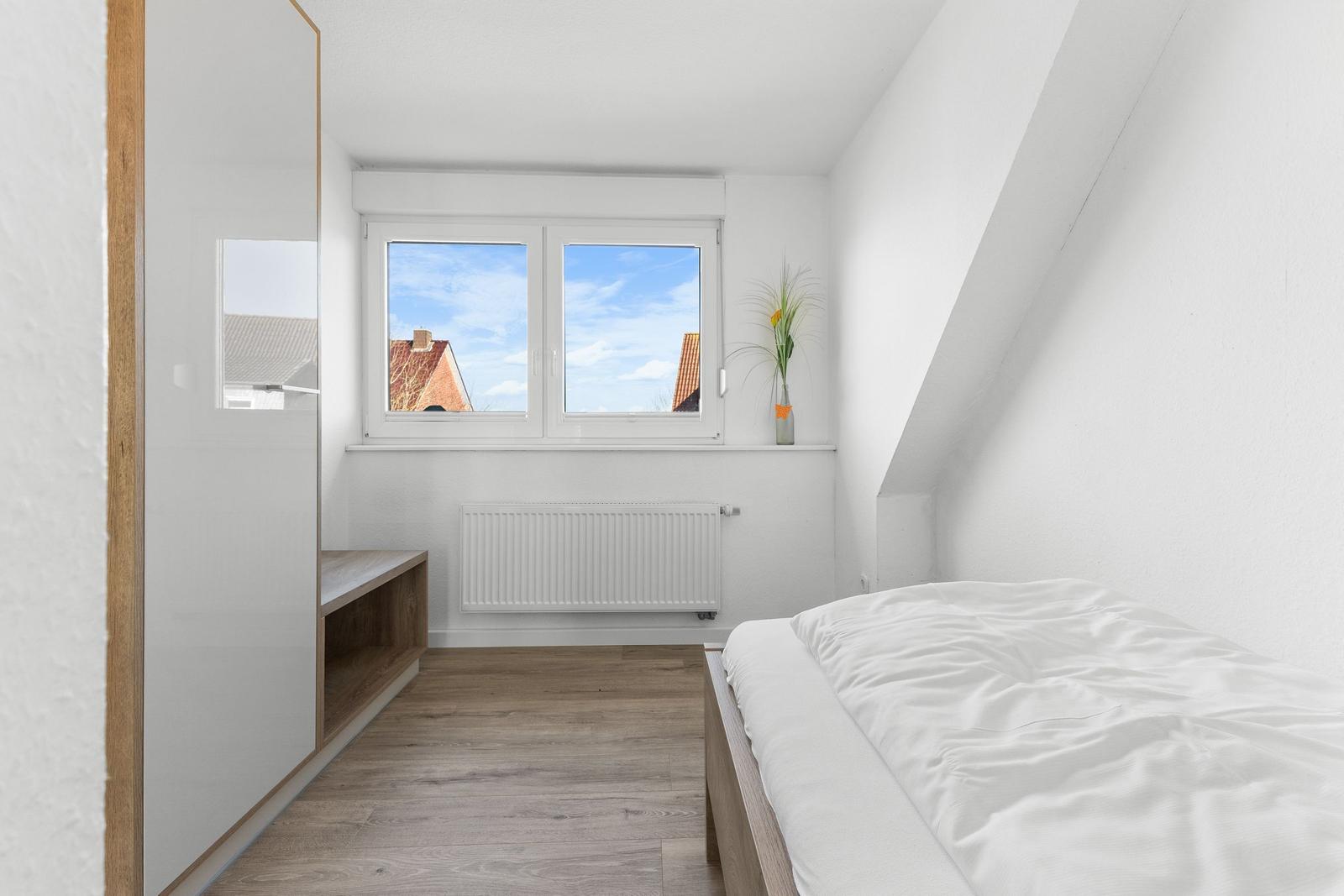 Schlafzimmer mit Dachschräge, Fenster und Bett. Holzfußboden und Schrank.