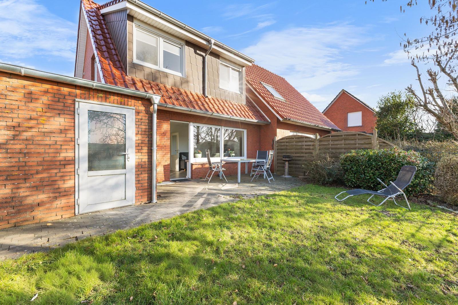 Haus mit Garten, Terrasse und Liegestuhl. Roter Ziegeldach und Backsteinmauer.