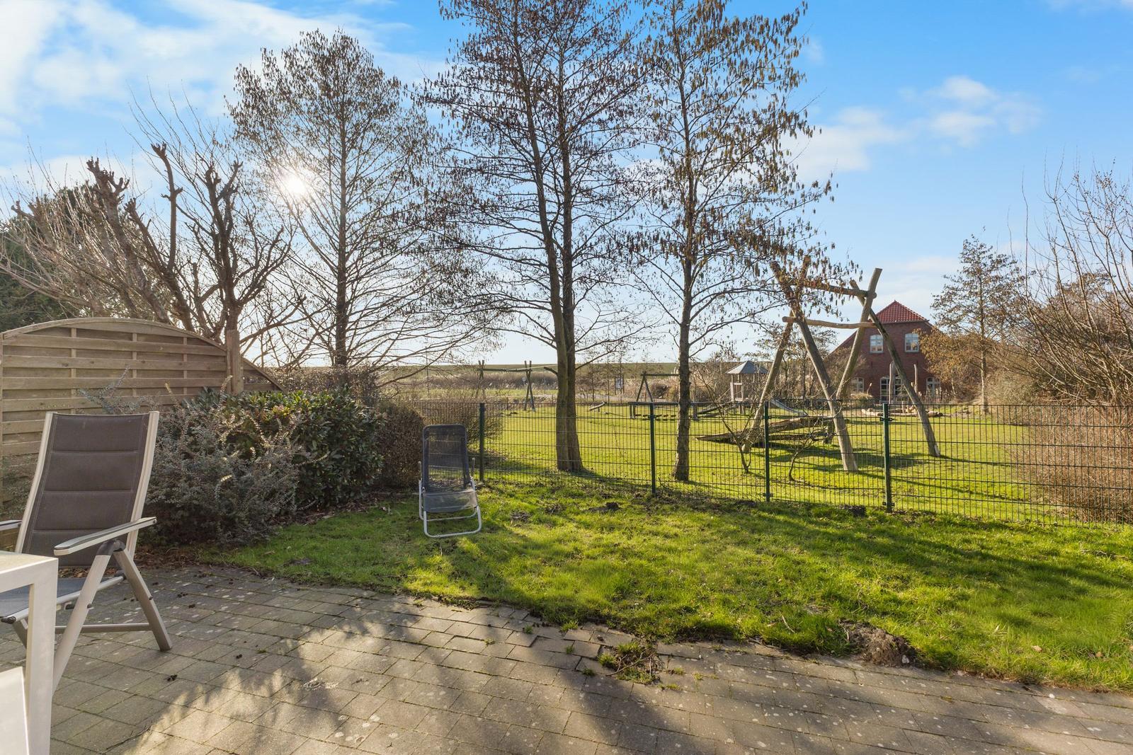 Terrasse mit Liegestühlen, umgeben von Grünfläche und Spielplatz im Hintergrund.