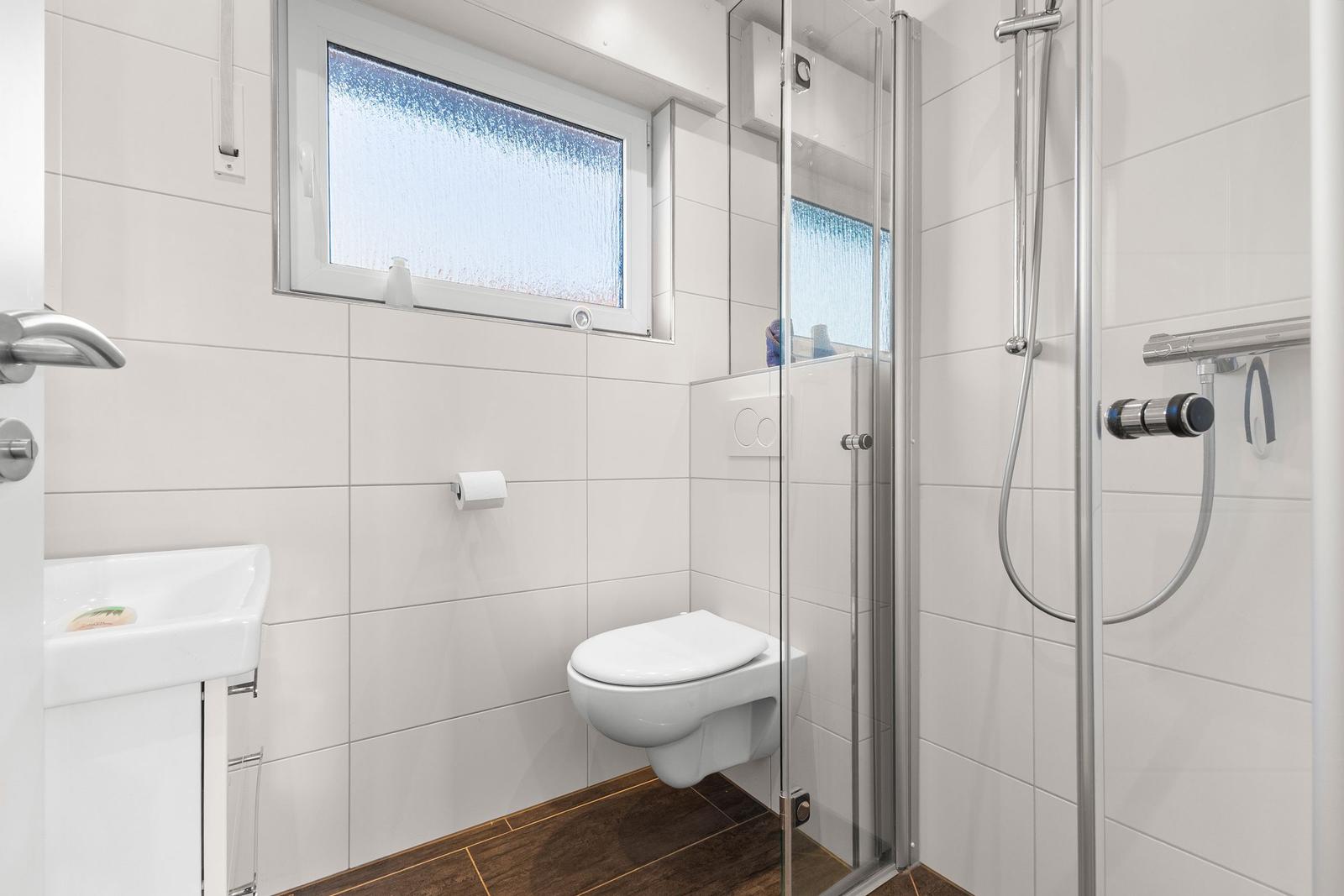 Badezimmer mit Dusche, WC und Waschbecken. Fenster mit getöntem Glas.