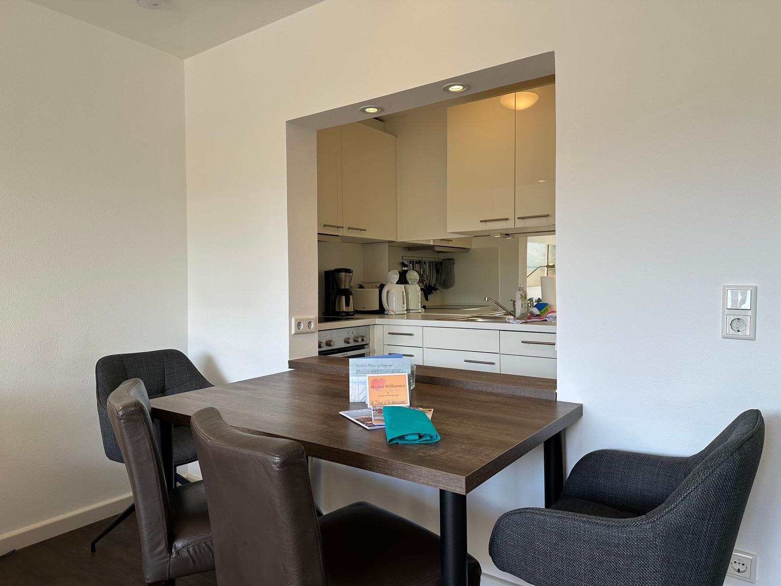 Dining area with table and chairs. Kitchen visible in the background.