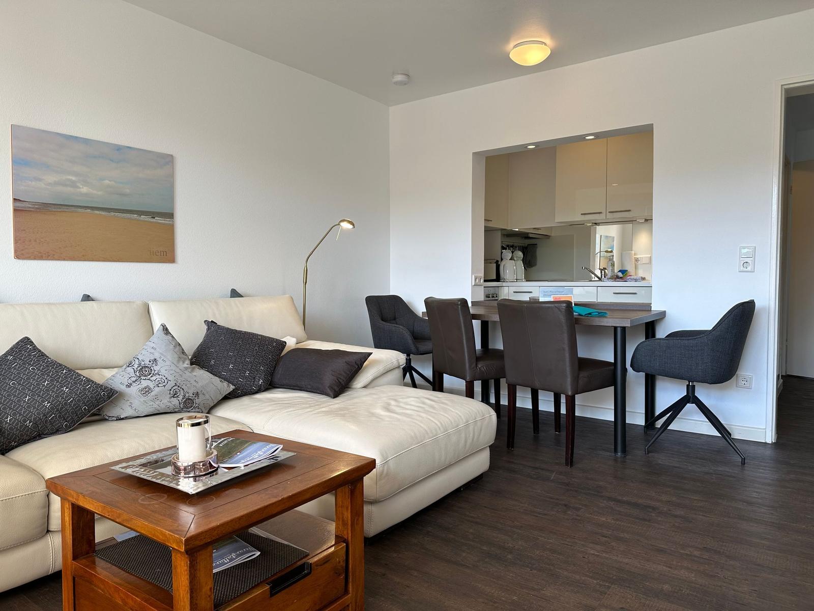 Living and dining area with sofa, table, and kitchen area in the background.