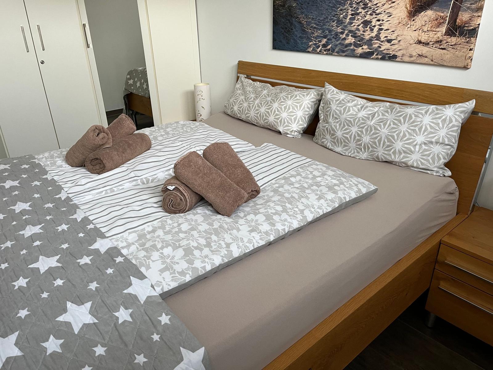 Doppelbett mit Bettwäsche und Handtüchern. Holzgestell und Wandbild.