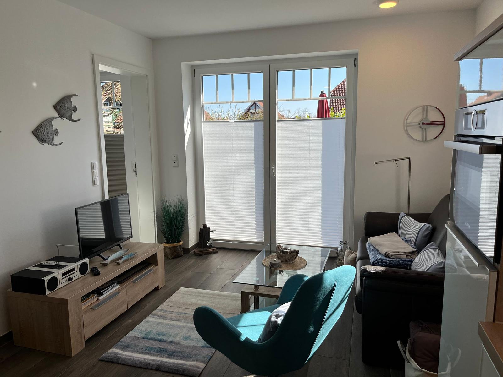 Wohnzimmer mit Sofa, blauer Sessel, TV und Glasfront zur Terrasse.