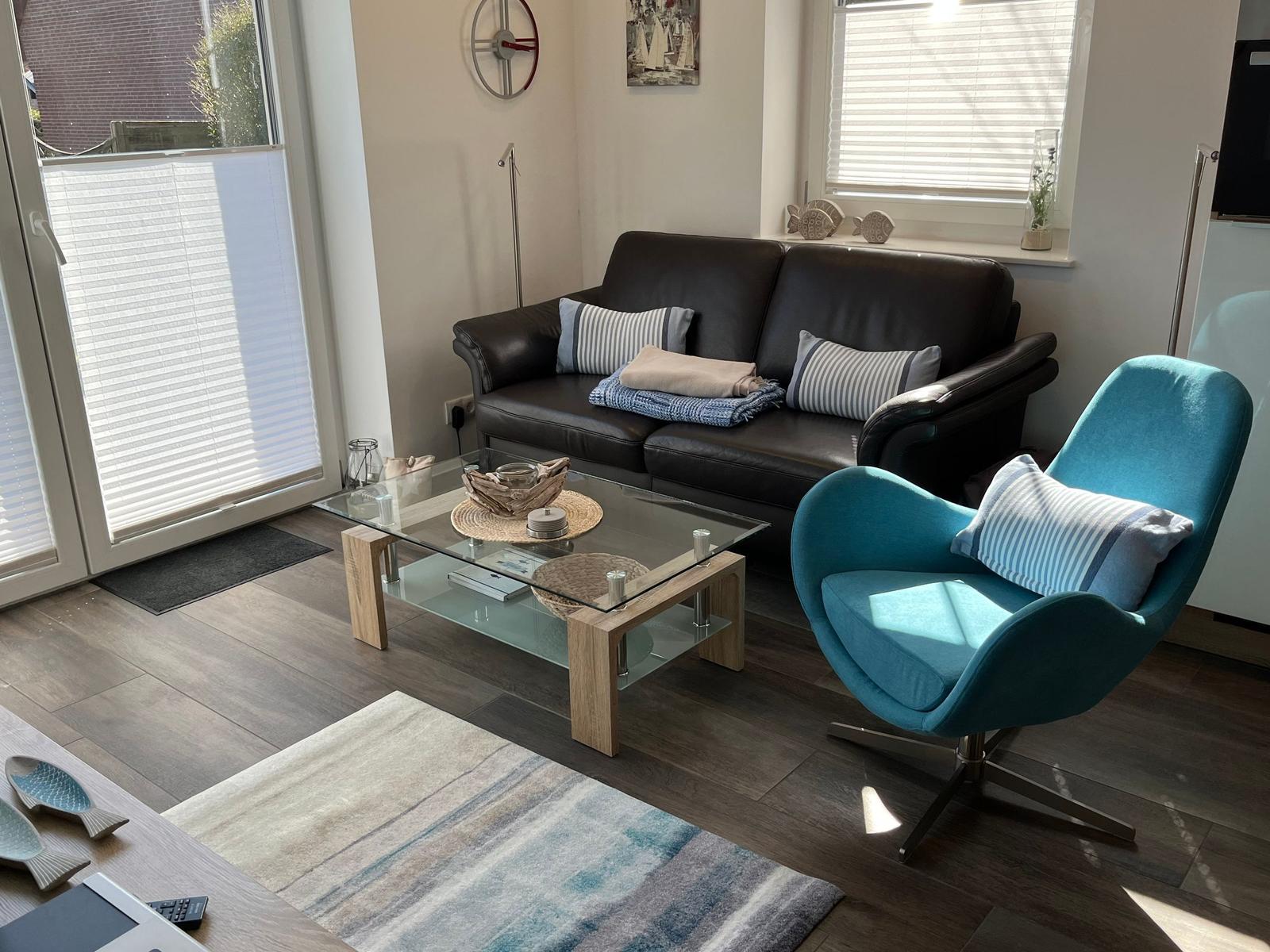 Ein Wohnzimmer mit braunem Sofa, blauem Sessel und Glas-Tisch.