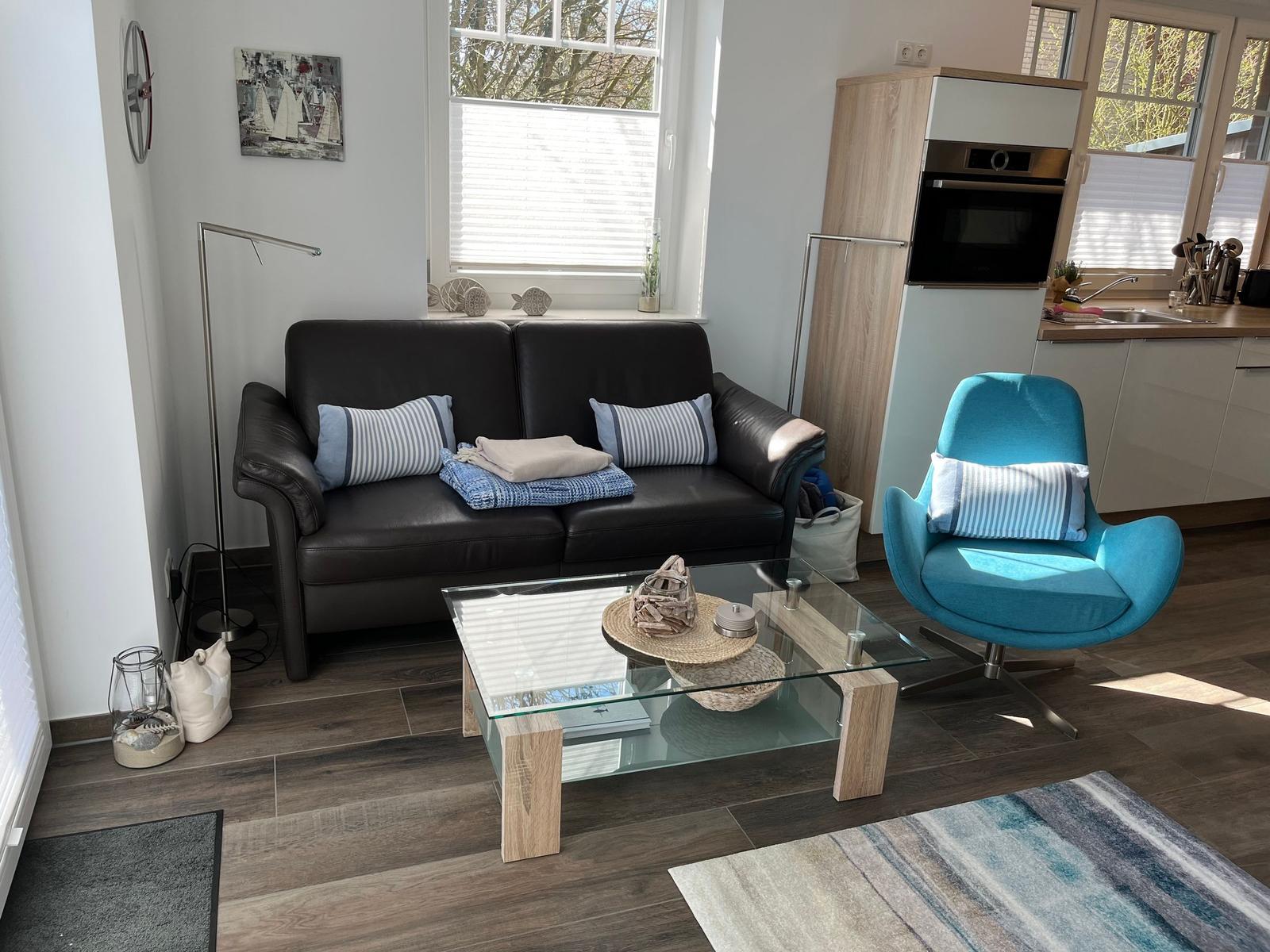 Ein Wohnbereich mit einem schwarzen Sofa, einem blauen Sessel und einem Glas-Tisch.