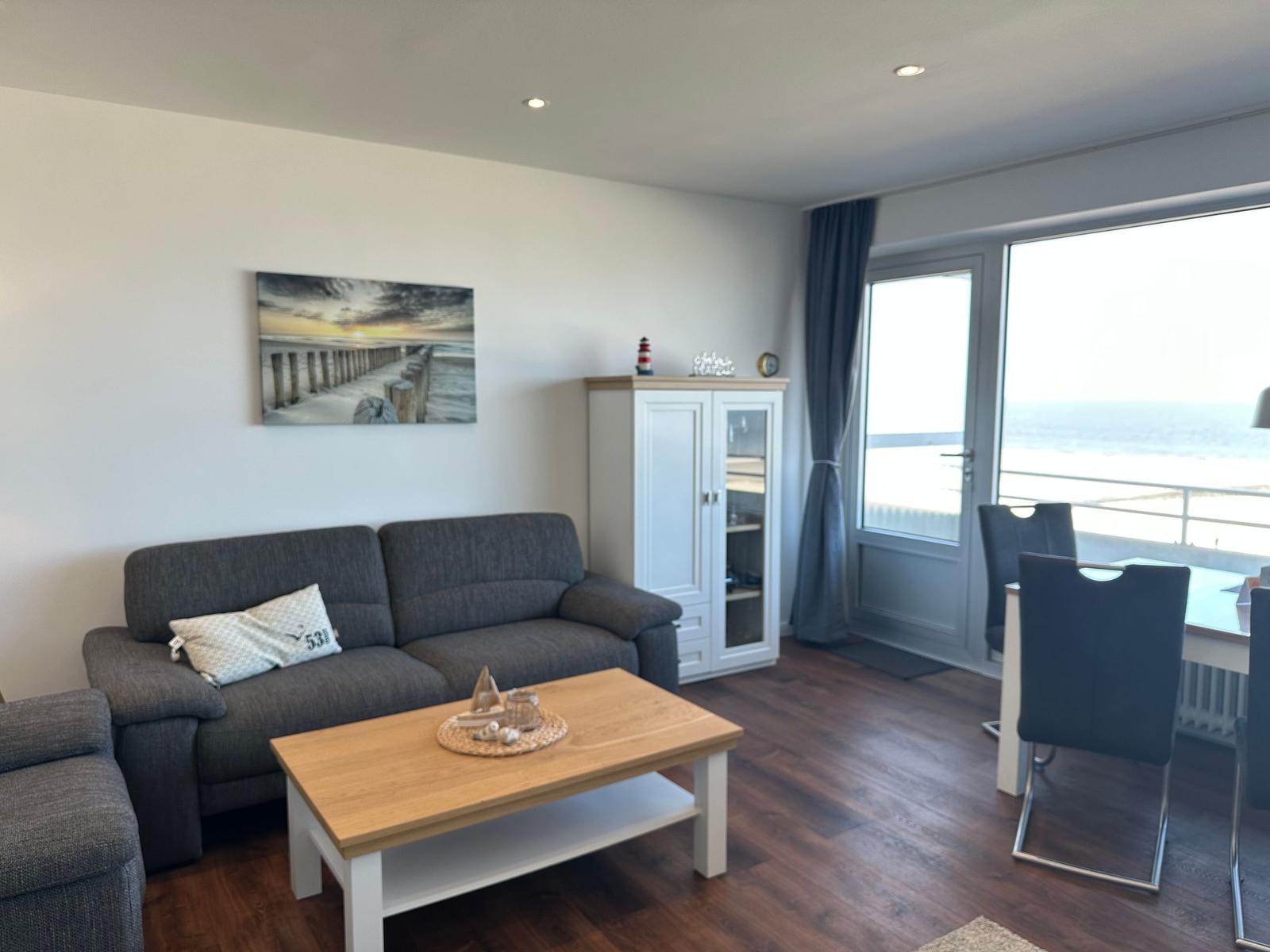 Wohn- und Essbereich mit Blick aufs Meer, grafe Sofa, Holztisch und weißer Sideboard.