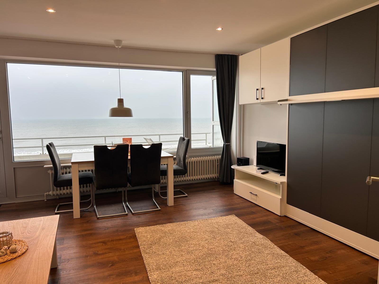 Wohn- und Essbereich mit Meerblick, Esstisch, TV und Holzboden.