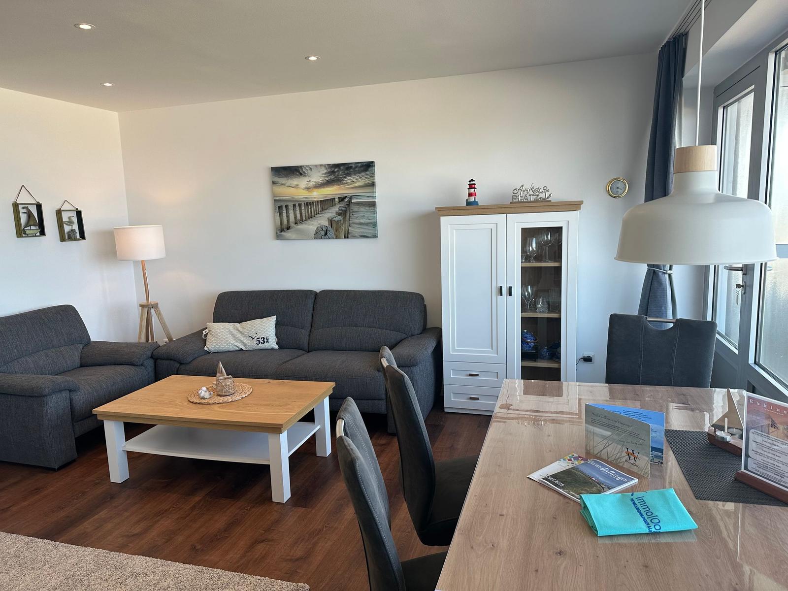 Wohn- und Essbereich mit Sofa, Esstisch und Küchenzeile. Wandbild und Schrank sind sichtbar.