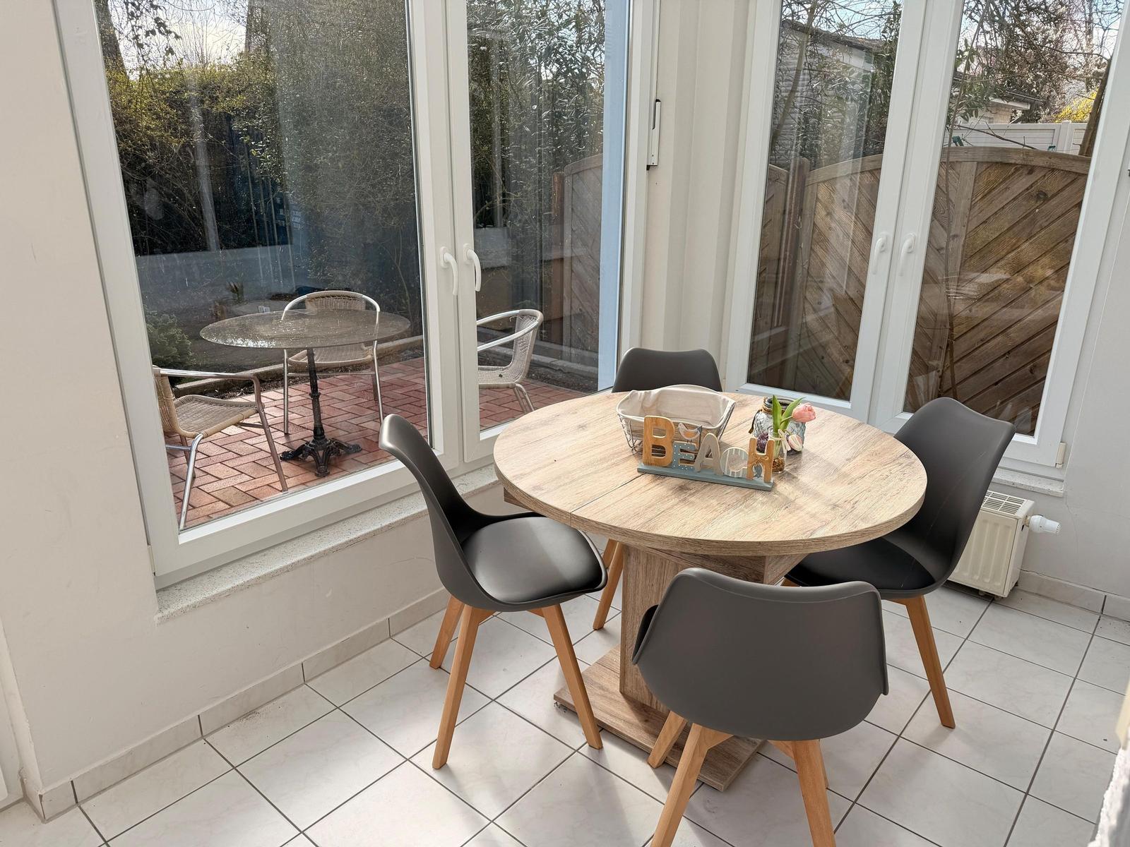 Runder Tisch mit vier Stühlen im Innenbereich, Blick auf Terrasse mit Tisch und Stühlen.