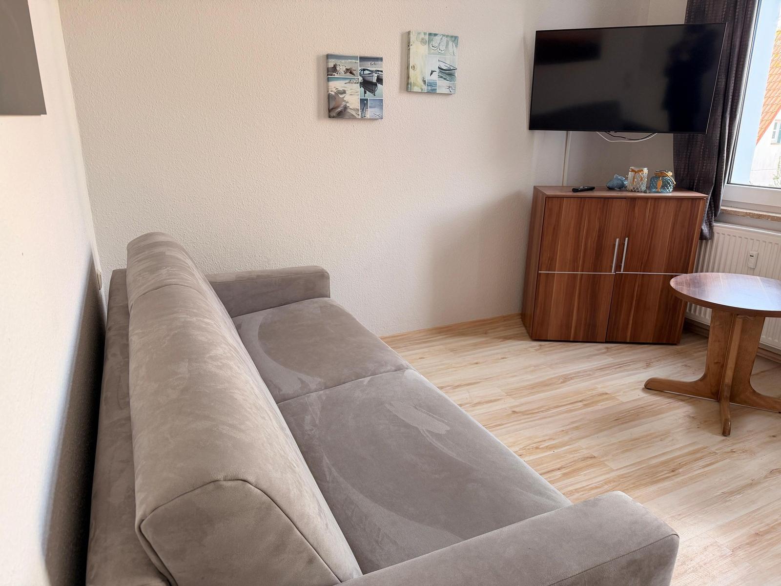 Ein Wohnzimmer mit einem grauen Sofa, einem Holztisch und einem Fernseher auf einem Schrank.